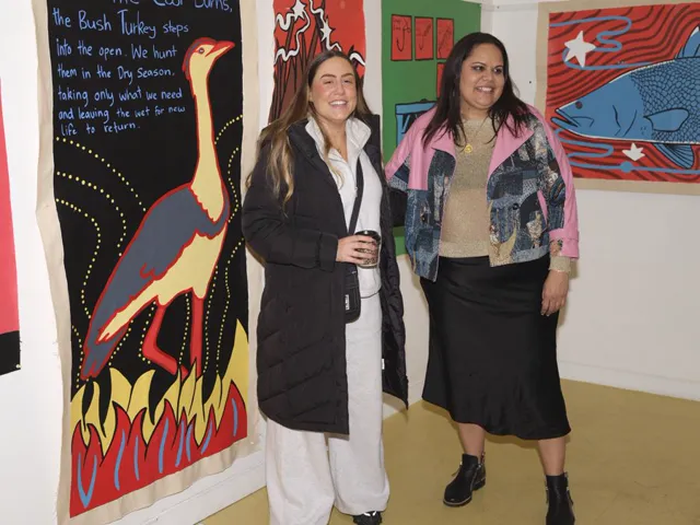 Two guests standing among large painted works on the walls of The Black Canoe gallery in Waterloo