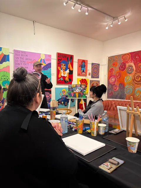 The artist talking the group through the painting, with works from the gallery walls behind