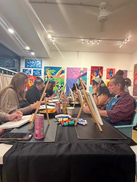 Guests listening at the painting table, blank canvases on easels in front of them