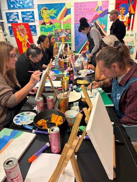 Guests at the table with paints, brushes and snacks, each working on a canvas