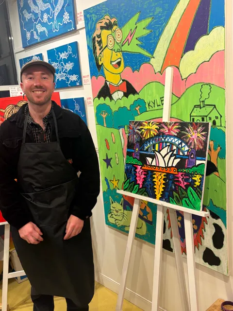 The artist standing beside his Sydney Harbour fireworks painting on an easel