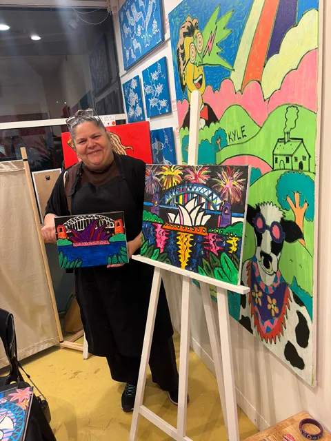 A guest laughing beside her finished painting and the fireworks painting