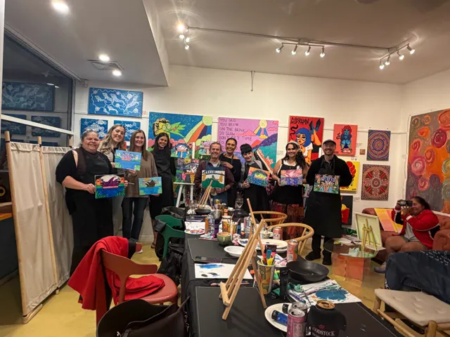 The group at The Black Canoe holding their finished paintings at the first Paint & Sip night